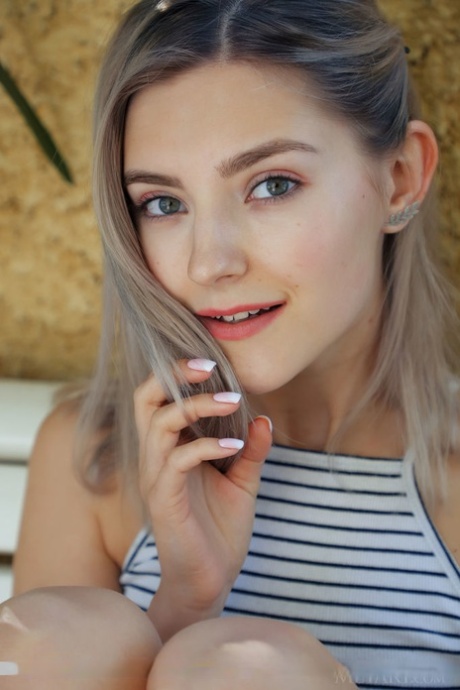 Petite teen Eva Elfie holds a flower while posing naked on a patio bench